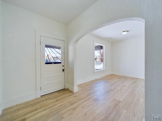 foyer entrance featuring arched walkways, a textured wall, light wood-style flooring, and baseboards