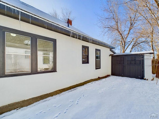 snow covered property featuring a storage shed, an outdoor structure, and stucco siding