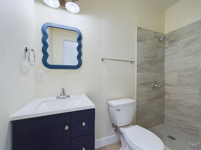 bathroom featuring toilet, baseboards, a tile shower, and vanity