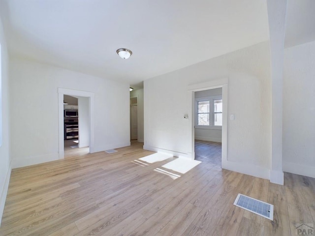 spare room featuring light wood finished floors, baseboards, and visible vents