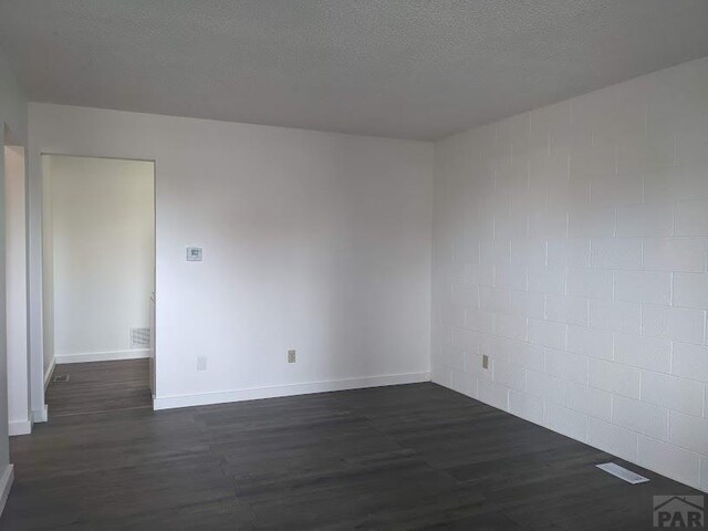 empty room featuring dark wood-style flooring, visible vents, a textured ceiling, and baseboards