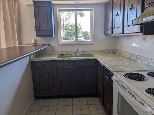 kitchen featuring white electric range oven, light countertops, a sink, dark brown cabinetry, and under cabinet range hood