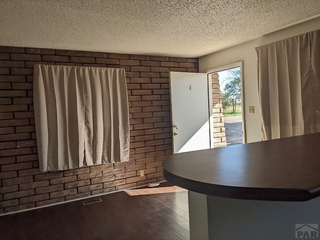 interior space featuring brick wall, visible vents, a textured ceiling, and wood finished floors