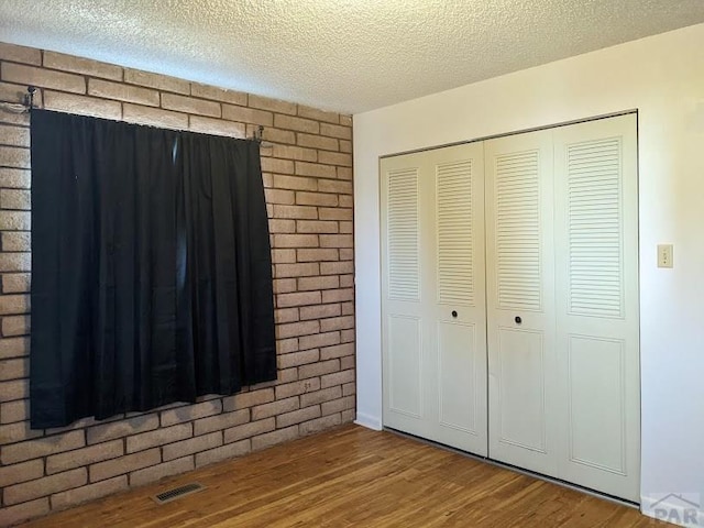 unfurnished bedroom with a closet, visible vents, a textured ceiling, and wood finished floors