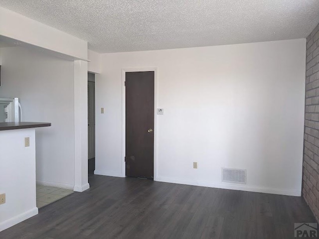 spare room with dark wood-type flooring, visible vents, a textured ceiling, and baseboards