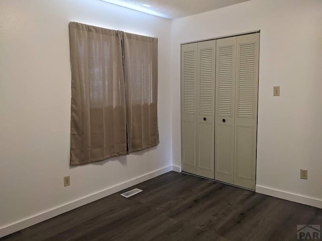 unfurnished bedroom featuring a closet, dark wood-style flooring, visible vents, and baseboards