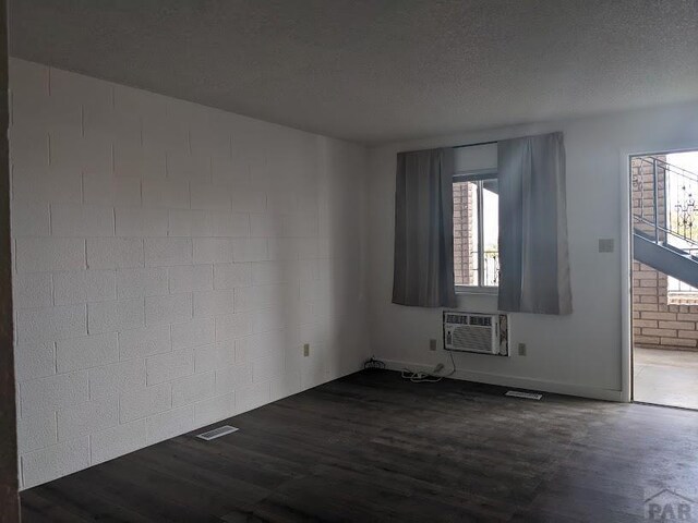 unfurnished room with dark wood-style floors, visible vents, a textured ceiling, and a wall mounted AC