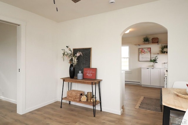 hallway featuring light wood-type flooring, a baseboard radiator, arched walkways, and baseboards