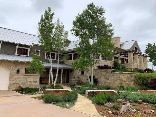 view of front facade with a standing seam roof, stone siding, a chimney, and metal roof