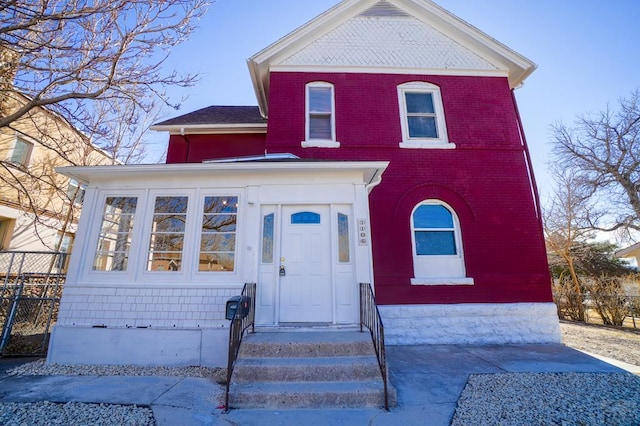 view of front of property with entry steps, brick siding, and fence