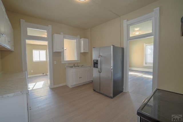 kitchen with range with electric cooktop, white cabinetry, light countertops, stainless steel fridge with ice dispenser, and light wood finished floors