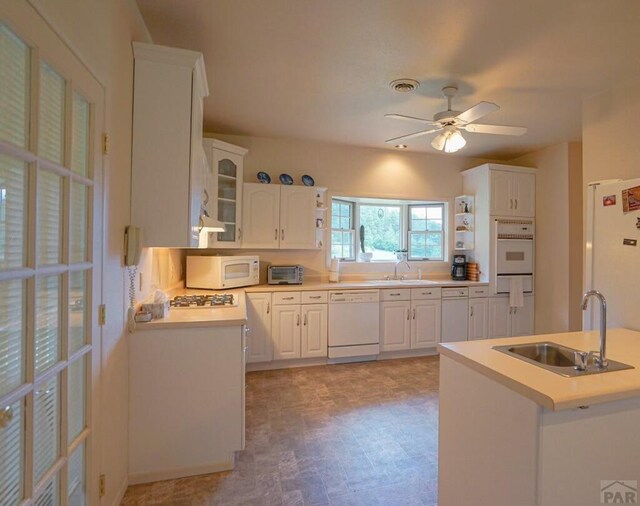 kitchen with white appliances, white cabinets, glass insert cabinets, light countertops, and a sink