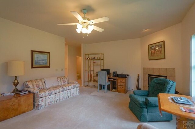 living area featuring a ceiling fan, a tile fireplace, and light carpet