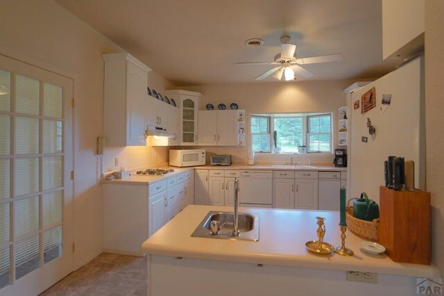 kitchen featuring white appliances, glass insert cabinets, light countertops, white cabinetry, and a sink