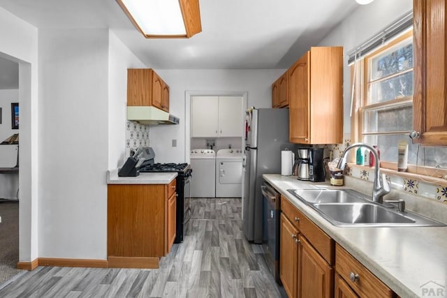 kitchen with a sink, washer and dryer, gas stove, and brown cabinets