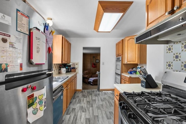 kitchen featuring light countertops, appliances with stainless steel finishes, under cabinet range hood, backsplash, and light wood-style flooring