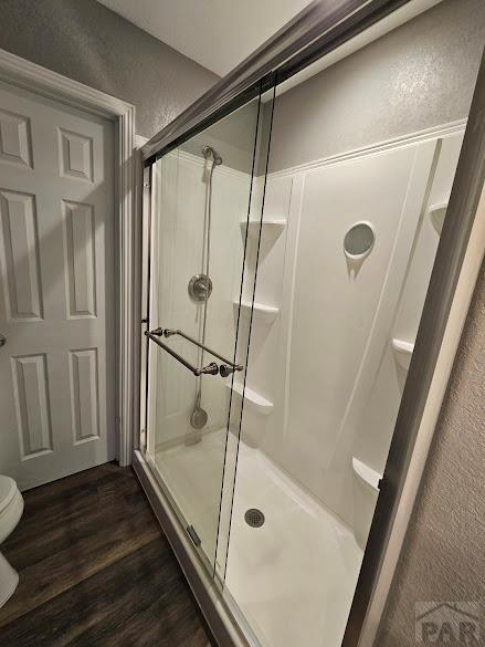 full bathroom featuring a textured wall, a shower stall, toilet, and wood finished floors