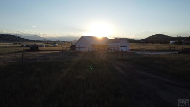 property exterior at dusk featuring a rural view, fence, and a mountain view