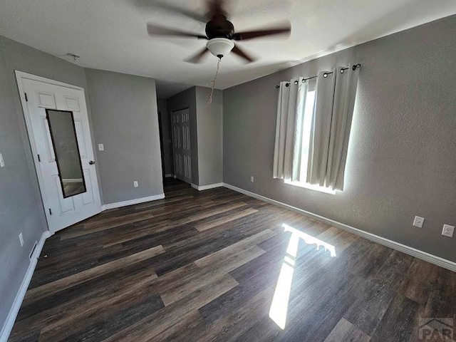 empty room with a ceiling fan, baseboards, and dark wood-style flooring