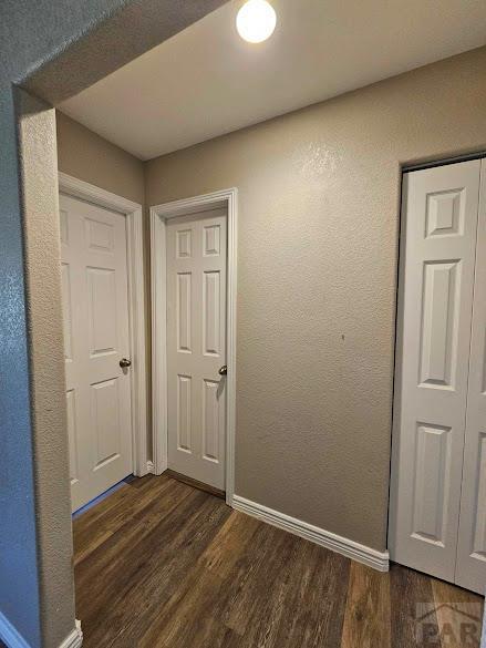 corridor with dark wood-style floors, a textured wall, and baseboards