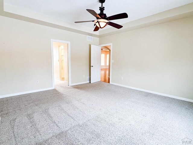 unfurnished bedroom featuring visible vents, baseboards, arched walkways, a raised ceiling, and carpet