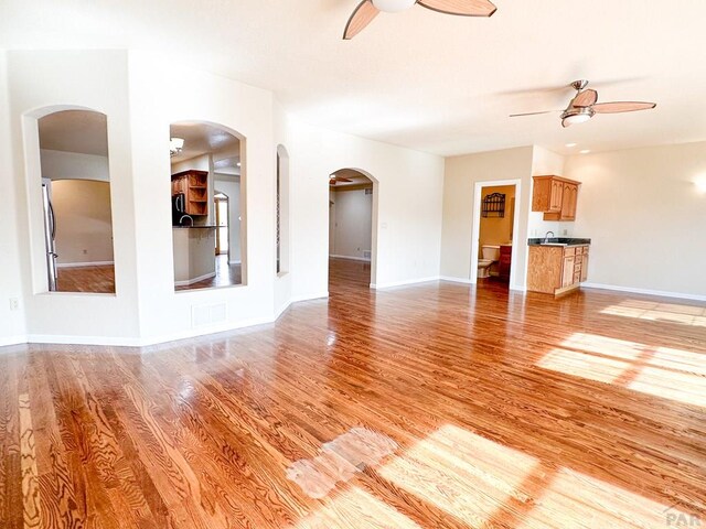 unfurnished living room featuring baseboards, a ceiling fan, and light wood-style floors