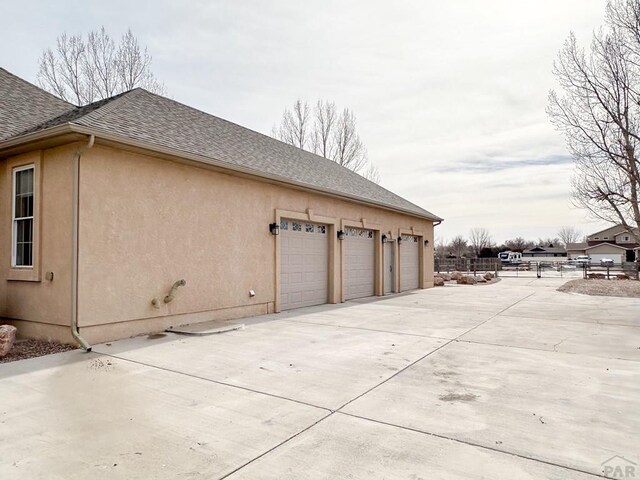 view of home's exterior featuring a garage, concrete driveway, roof with shingles, and stucco siding