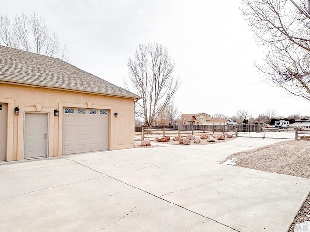 view of home's exterior with a garage, a shingled roof, an outbuilding, fence, and stucco siding