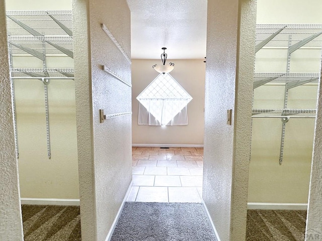 hall featuring baseboards, a textured ceiling, and a textured wall