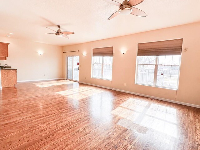 unfurnished living room with visible vents, light wood-type flooring, a ceiling fan, and baseboards