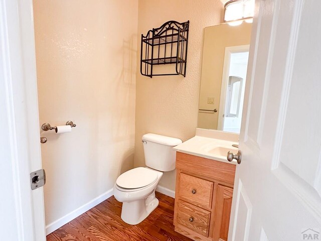 half bath with baseboards, vanity, toilet, and wood finished floors