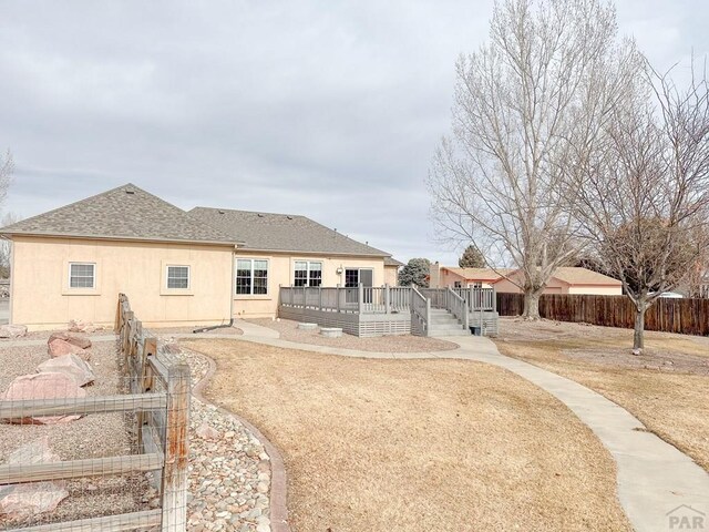 rear view of property with a shingled roof, fence, a wooden deck, and stucco siding