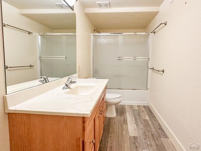 bathroom with visible vents, bath / shower combo with glass door, toilet, wood finished floors, and vanity