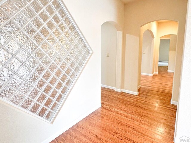 corridor with arched walkways, wood finished floors, and baseboards