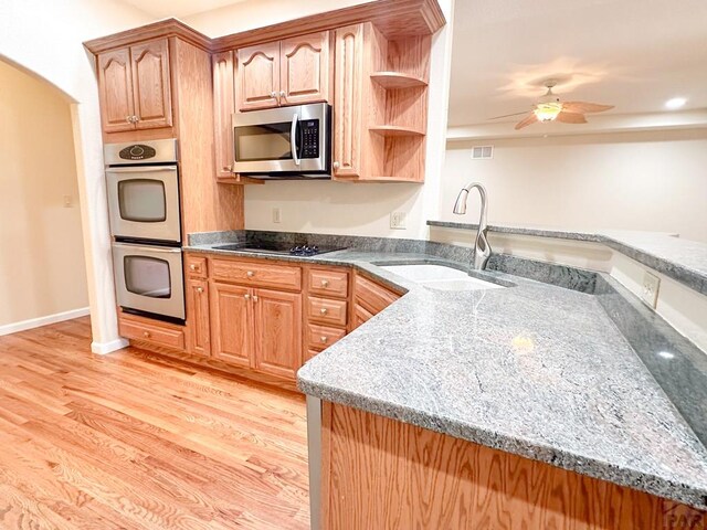 kitchen with light wood finished floors, appliances with stainless steel finishes, dark stone countertops, and a sink