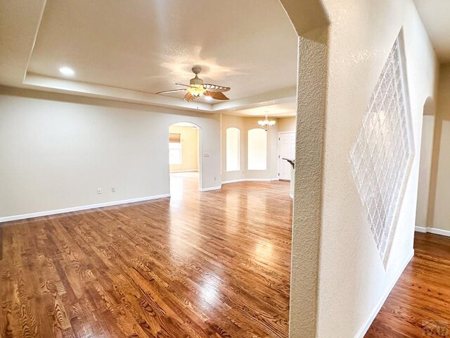 unfurnished living room featuring a tray ceiling, arched walkways, and wood finished floors