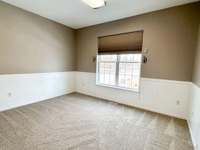 empty room with carpet floors, a wainscoted wall, and visible vents