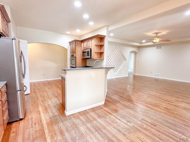 kitchen with arched walkways, brown cabinets, open shelves, stainless steel appliances, and visible vents