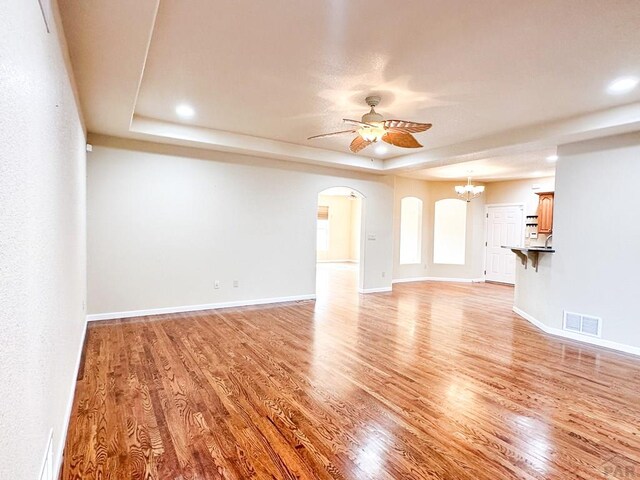 unfurnished living room featuring a tray ceiling, visible vents, ceiling fan, and light wood finished floors