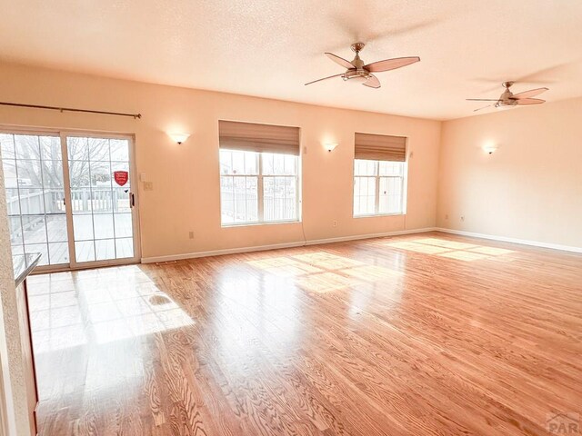 interior space with light wood-style floors, ceiling fan, baseboards, and a textured ceiling