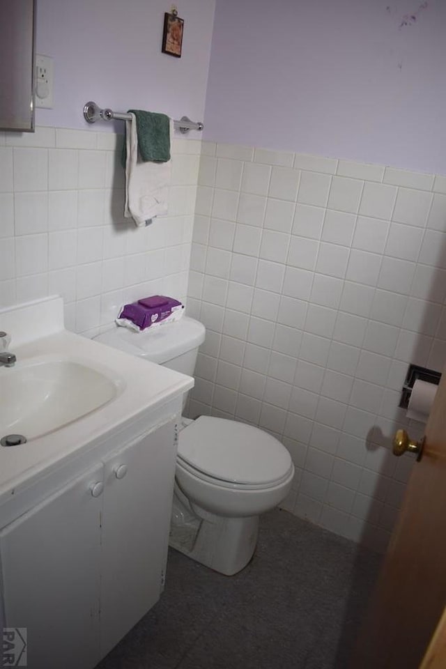 half bath featuring vanity, tile walls, and toilet