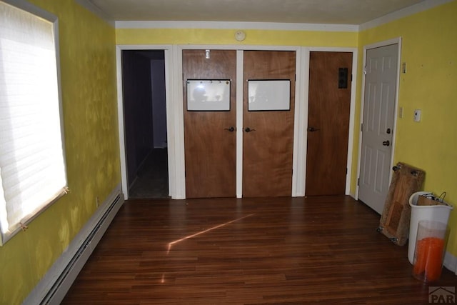 unfurnished bedroom with a baseboard heating unit, wood finished floors, and multiple closets