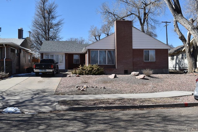 view of front of house featuring brick siding, driveway, and a chimney