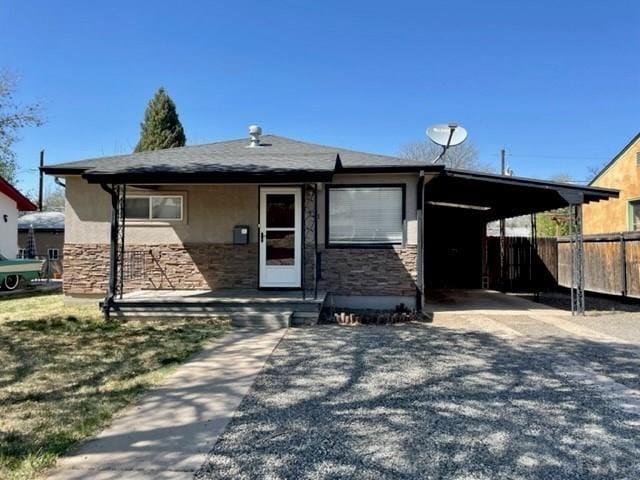 view of front of home featuring stone siding, an attached carport, gravel driveway, fence, and stucco siding