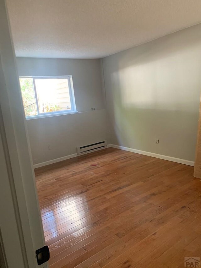 unfurnished room with a baseboard radiator, a textured ceiling, baseboards, and wood finished floors