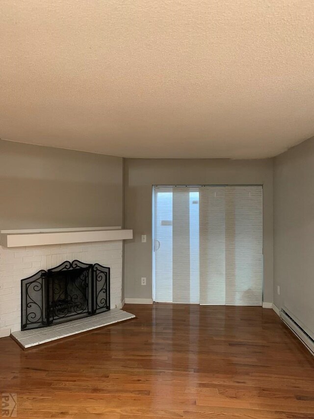 unfurnished living room featuring a baseboard radiator, a brick fireplace, a textured ceiling, wood finished floors, and baseboards