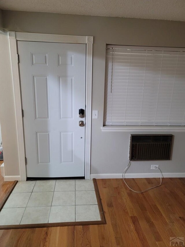 foyer entrance featuring light tile patterned floors, baseboards, a textured ceiling, and a wall mounted air conditioner