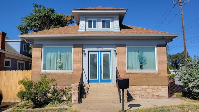 view of side of home featuring french doors, brick siding, roof with shingles, and fence