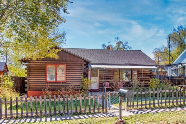 log cabin featuring a fenced front yard, a chimney, and log siding