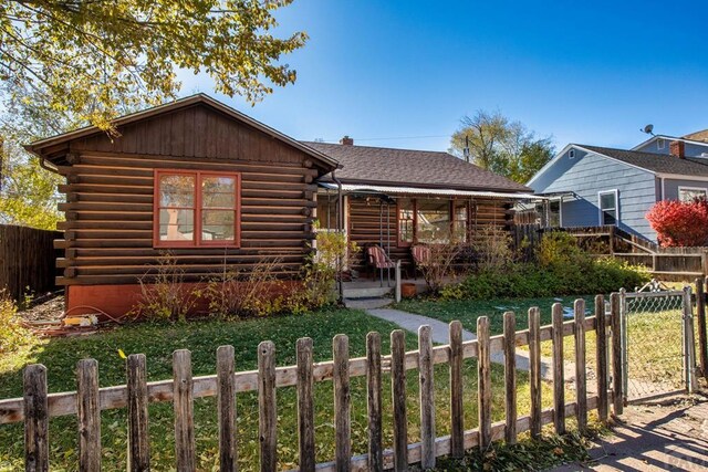 log-style house featuring log siding, roof with shingles, a gate, fence, and a front yard